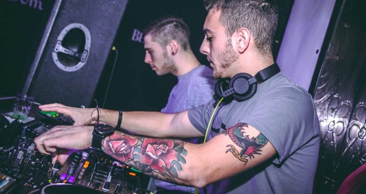 Two male DJs collaborating in a club booth