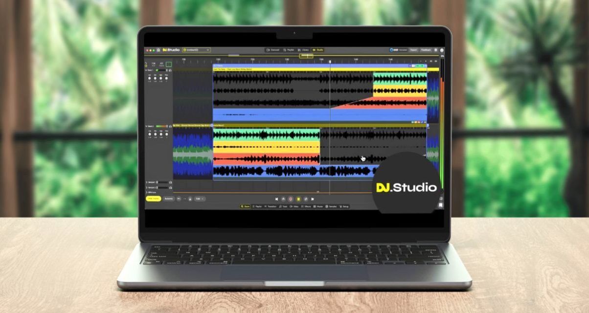 A silver laptop displaying DJ.Studio software sits on a wooden desk in front of a scenic background
