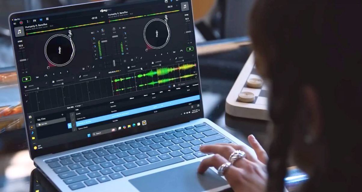 A white person using a silver PC with Djay Pro 5 software on the screen.