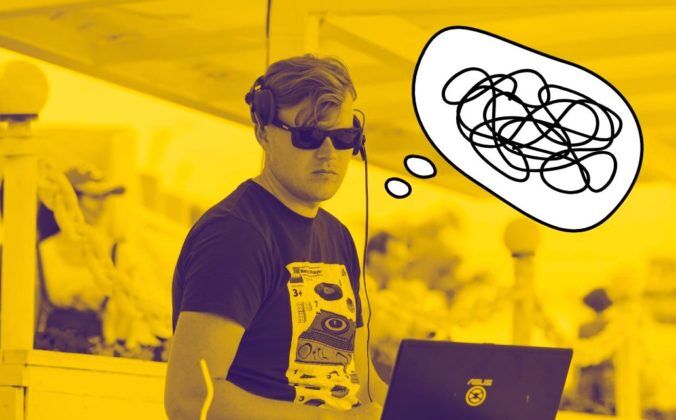 Photo of a tall white man standing behind a laptop. He has short hair and is wearing headphones, a dark t-shirt and sunglasses. The photo is saturated with a yellow colour. Next to his head there is a comic-style thought bubble. Inside the bubble is a bunch of squiggly lines, indicating confusion.