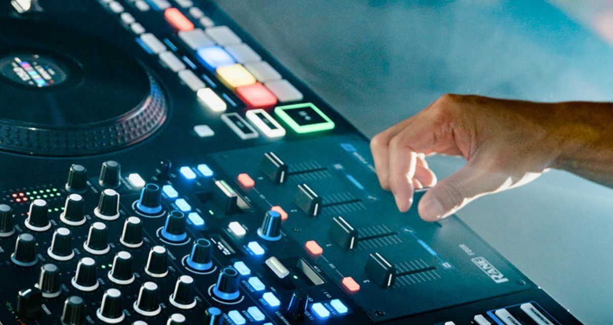The right hand of a white DJ uses the crossfader on a Rane Four controller in a foggy setting.