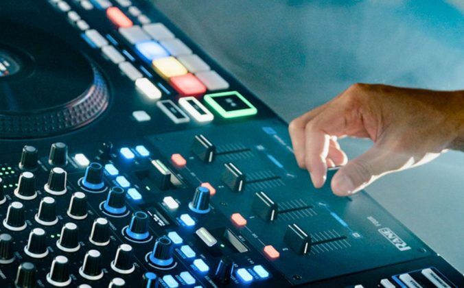 The right hand of a white DJ uses the crossfader on a Rane Four controller in a foggy setting.
