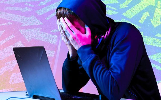 A composite image. In the foreground is a cutout of a younger white person sitting in front of their grey laptop with their head in their hands. They are wearing a shiny midnight blue hoodie with the hood covering their short brunette hair. Around their neck is a pair of headphones. The lighting in the room reflects off their hands and face in pink and blue hues. The background image is a semi-transparent rainbow gradient depicting a straight road down the middle. On each side of the road you can see a variety of arrows pointing in all different directions.