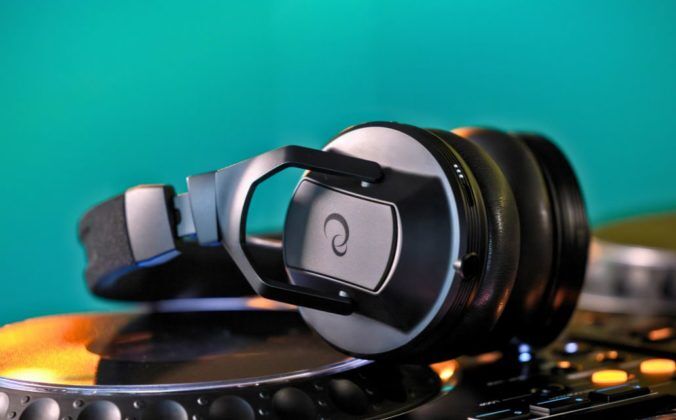 A pair of black AlphaTheta HDJ-F10 headphones laying across a CDJ-style media player. The wall in the background is emerald green.