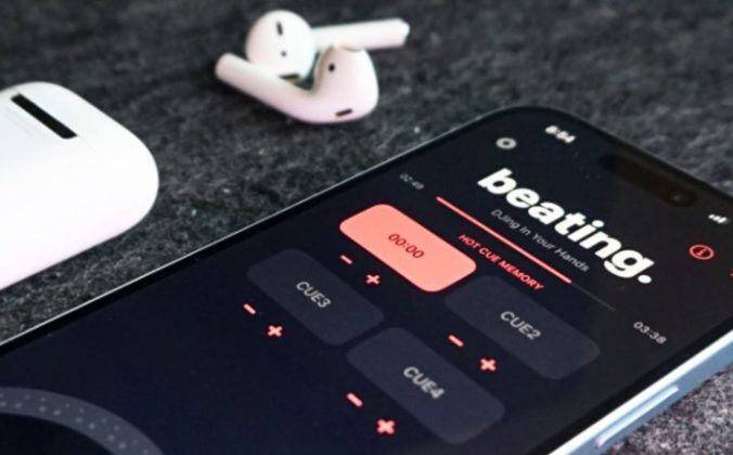 An iPhone sits next to a pair of AirPods on a grey surface. The phone is displaying a DJ app called "beating.", which has a black, dark grey, and light red colour scheme.